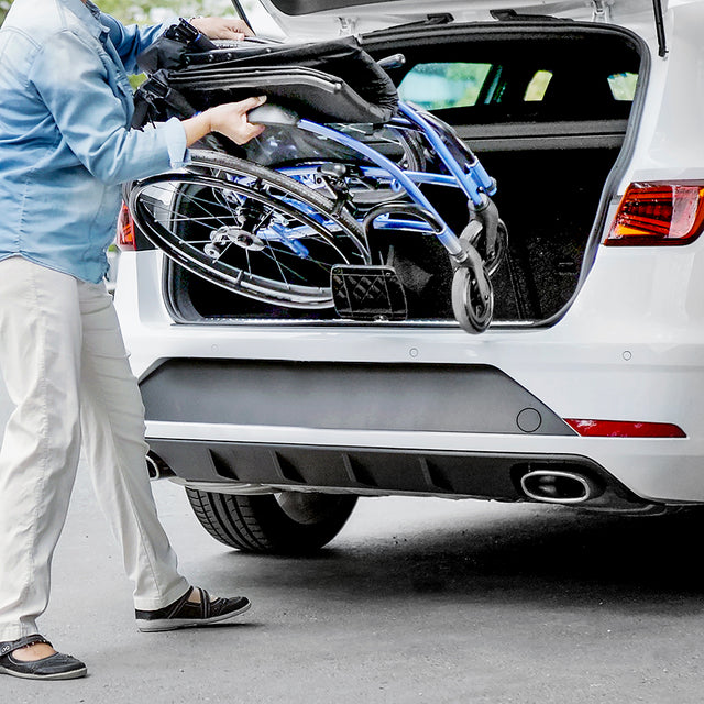 Person loading folded STRONGBACK 24AB Transport Wheelchair 1007AB into the back of a white car