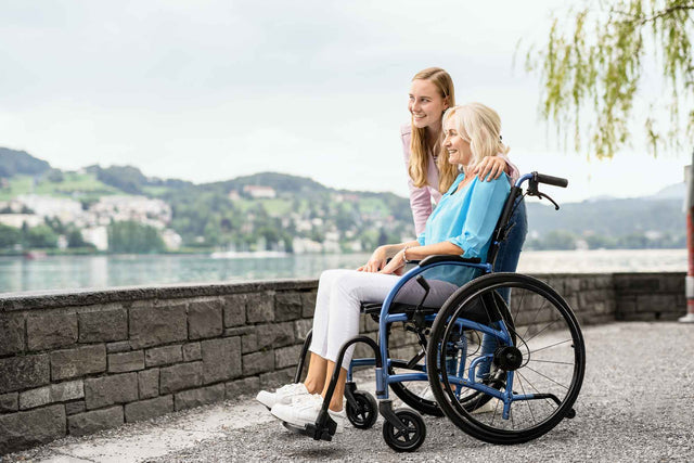 Elderly woman in a STRONGBACK 24AB Transport Wheelchair 1007AB by StrongBack Mobility with caregiver by the lakeside