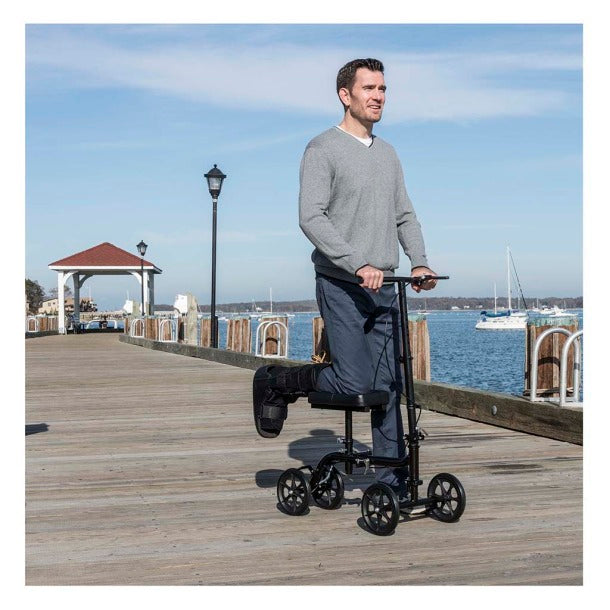 Drive Medical Economy Folding Knee Walker RTL799 in black, used by a man on a boardwalk