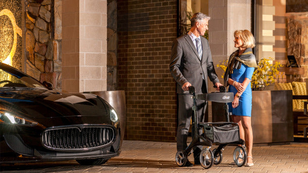 Drive Medical Nitro Elite CF Carbon Fiber Walker Rollator used by a man in a suit standing outdoors near a luxury car