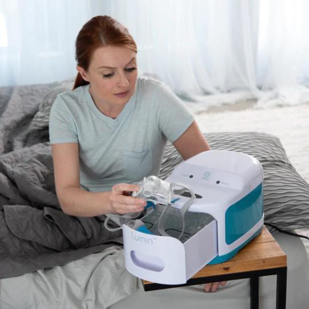 Woman using React Health Lumin UV-C Household Sanitizer on clear face shield on bed