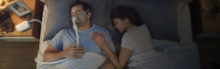 Man using Resmed AirMini AutoSet Portable CPAP machine while sleeping next to partner in bed
