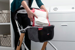 Trust Care Lets Go Indoor Rollator Walker with sturdy frame and storage bag holding folded laundry in a laundry room