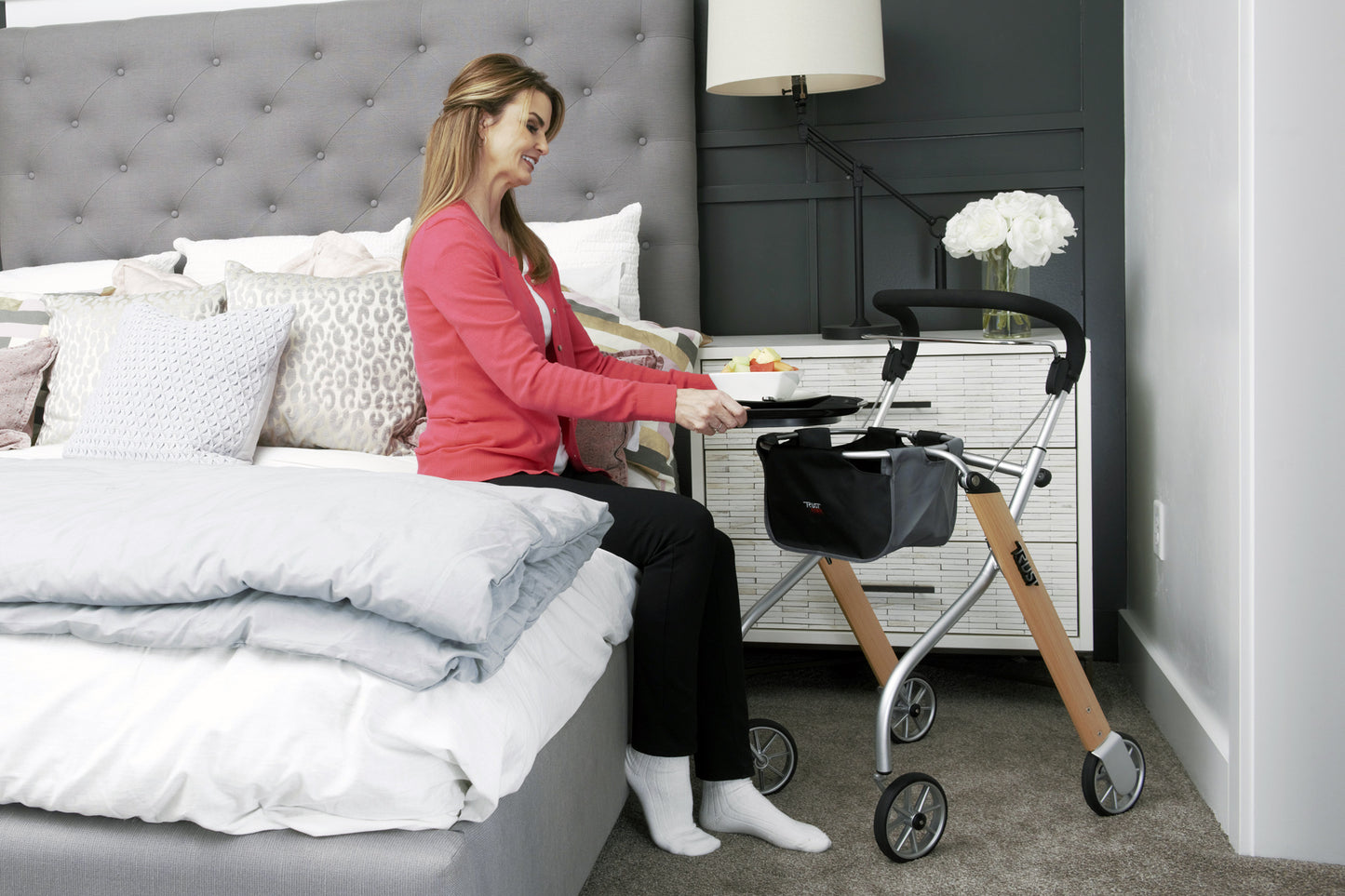 Woman using Trust Care Lets Go Indoor Rollator Walker next to bed for support and mobility