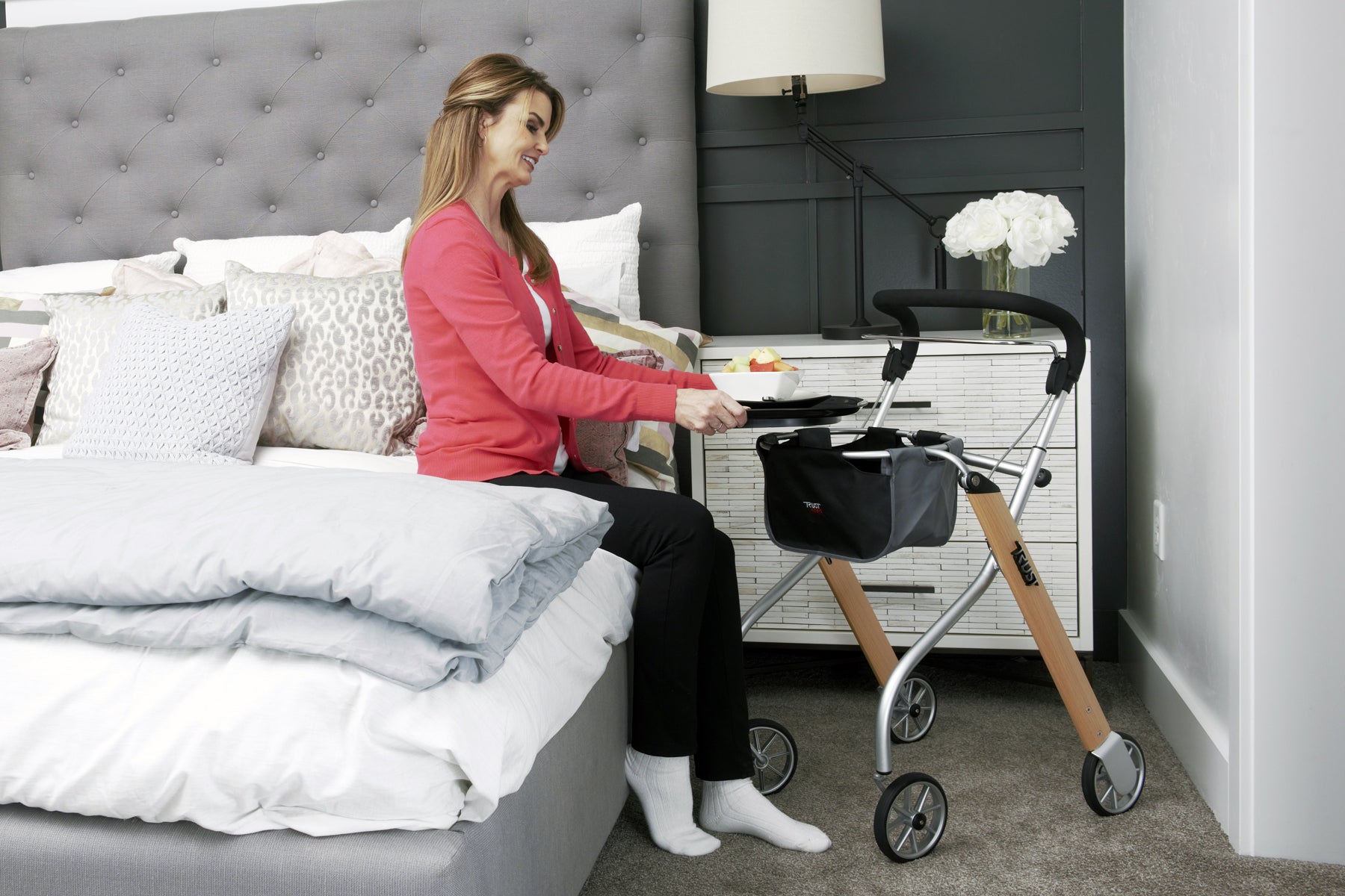 Woman using Trust Care Lets Go Indoor Rollator Walker next to bed for support and mobility