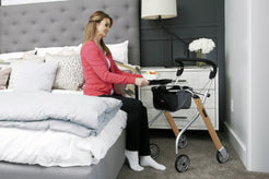 Woman using Trust Care Lets Go Indoor Rollator Walker next to bed for support and mobility